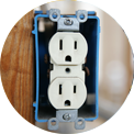 Blue electrical outlet box with a white double outlet, attached to a wooden wall.
