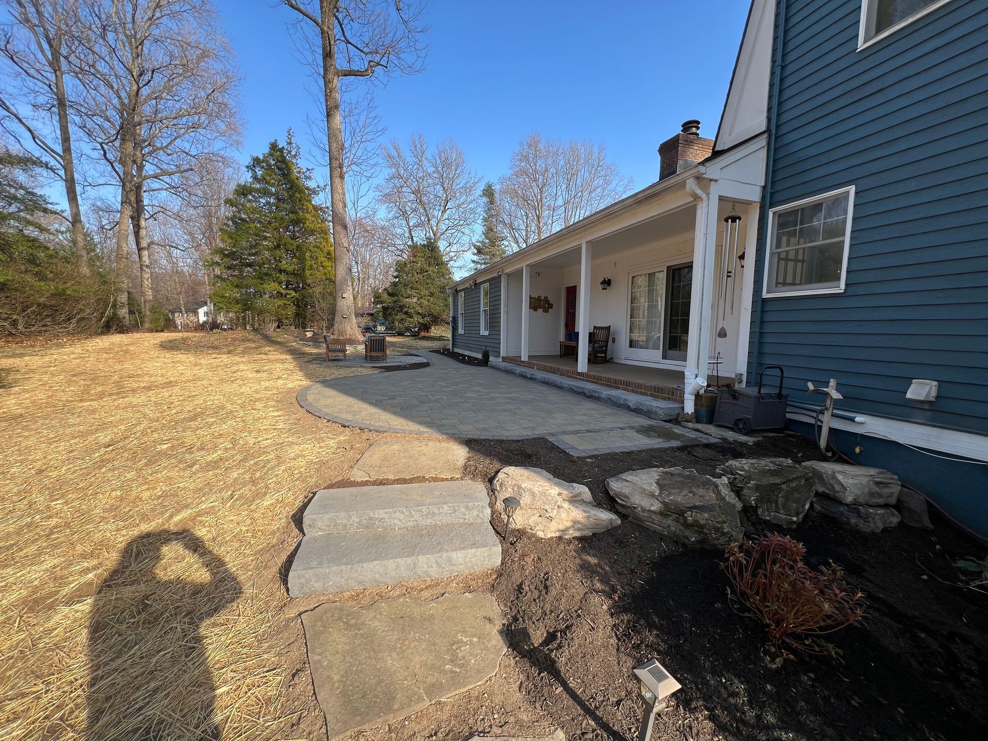 Stone steps leading to a gray patio with a white porch and blue house, surrounded by trees.