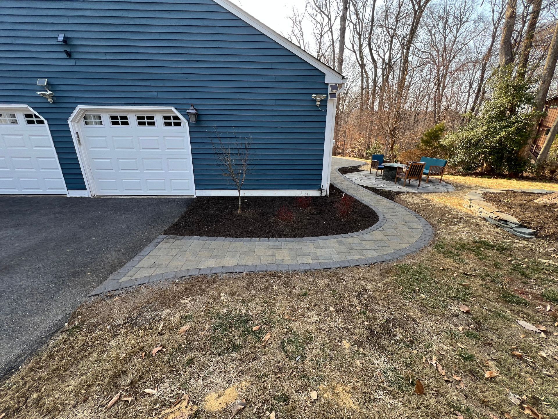 Blue garage with white doors, walkway, and landscaping along the side.