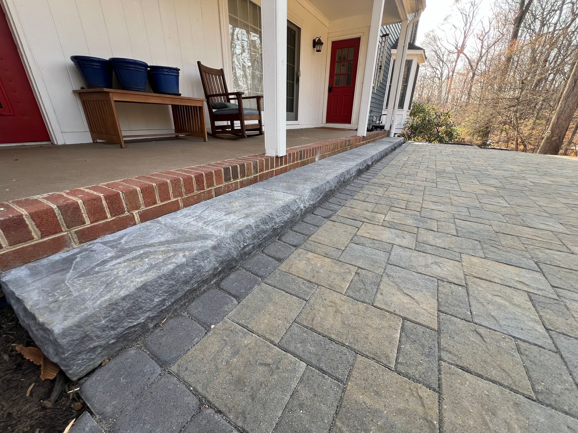 Brick and stone patio with a gray stone wall and the edge of a house.