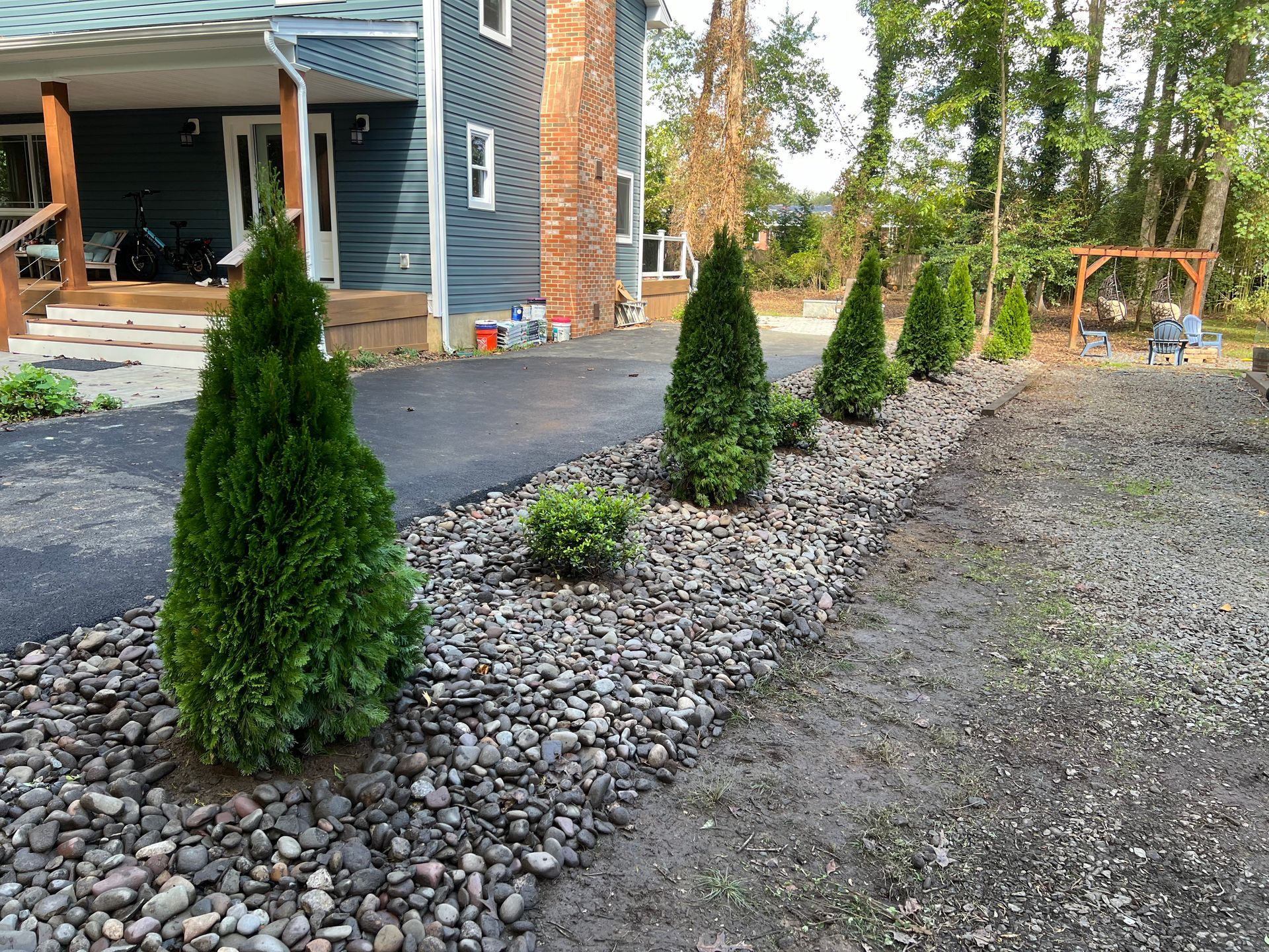 A blue house with a black driveway and line of evergreens in a gravel bed.