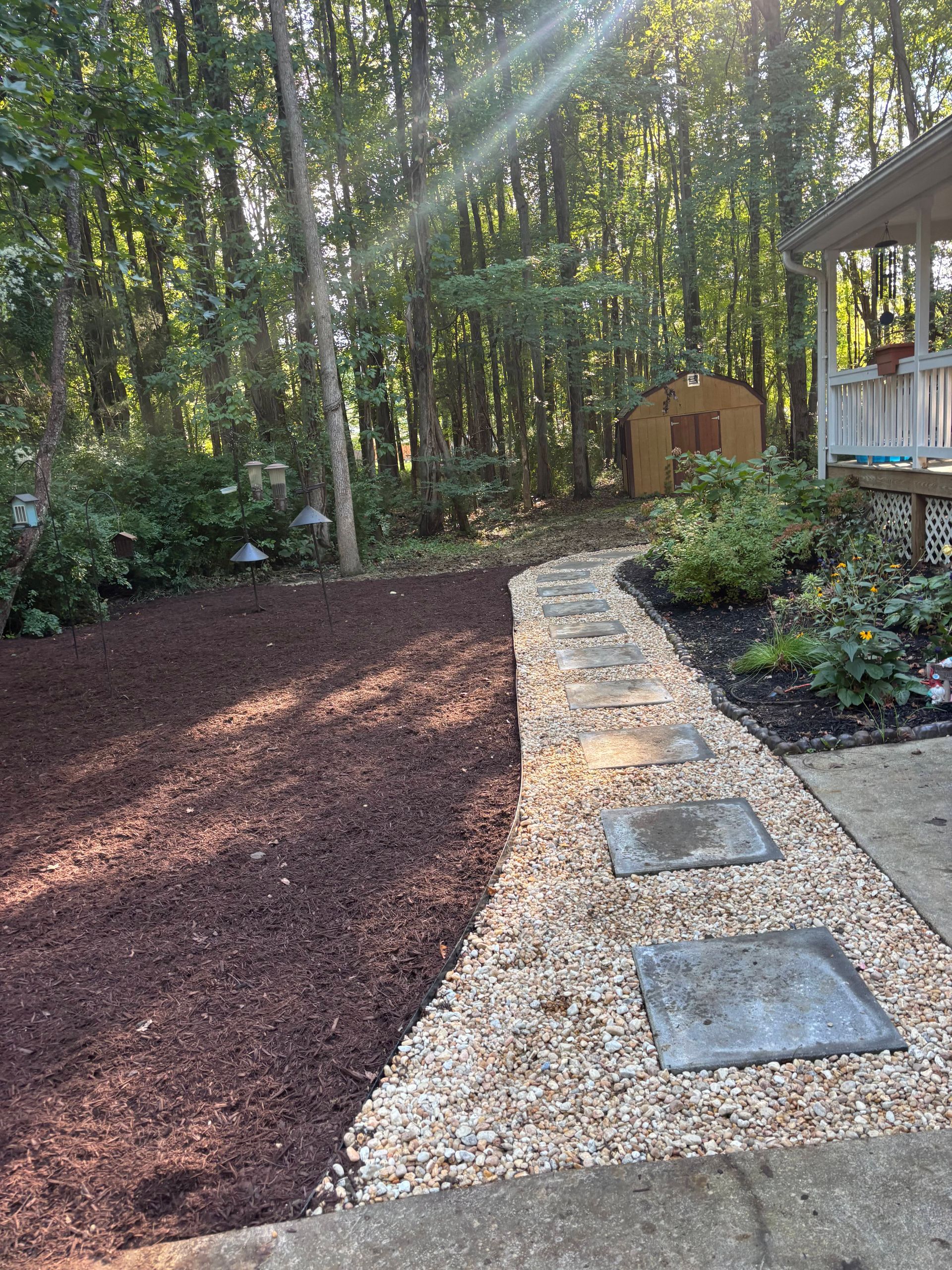 Stone path through backyard, leading to shed. Mulched area on left. Green foliage and porch on right.