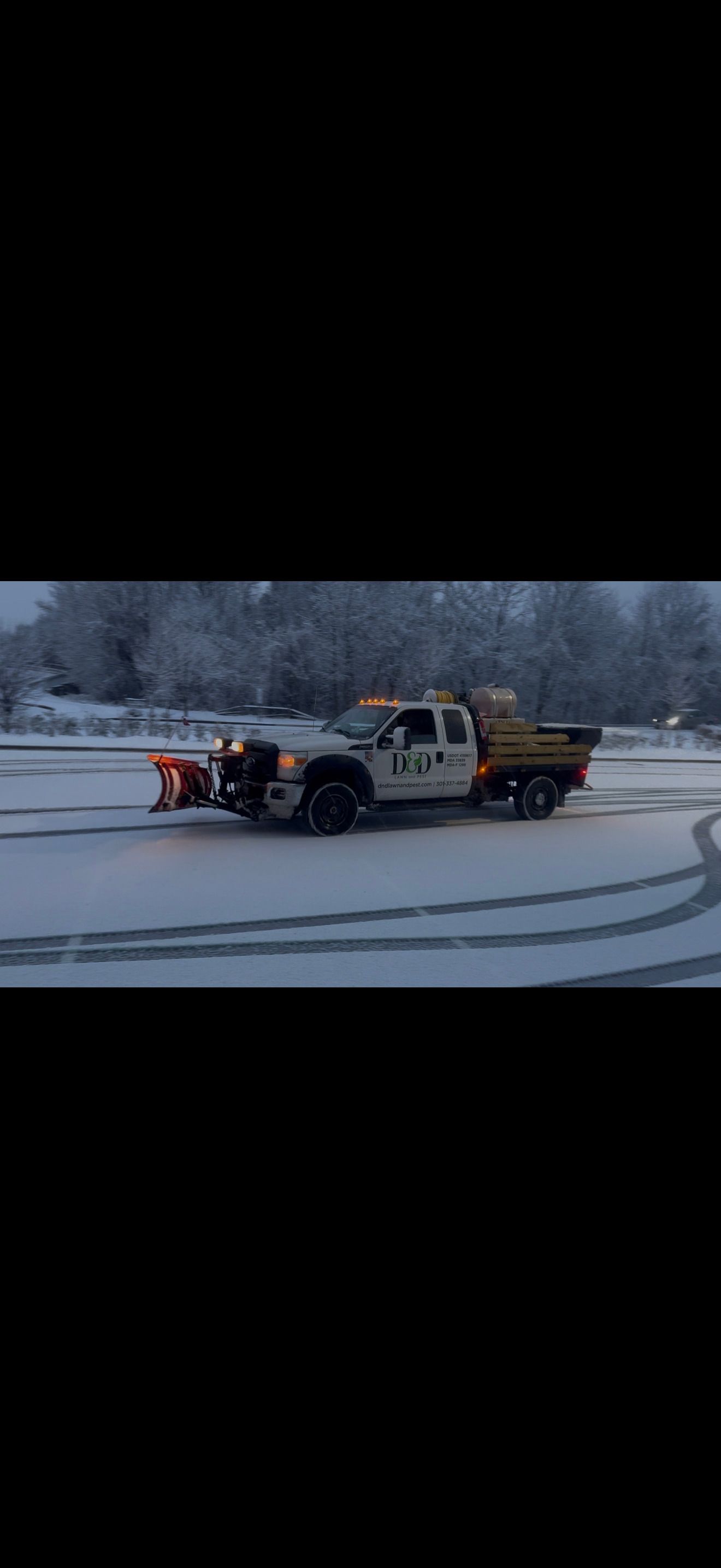 Snowplow truck plowing snow-covered parking lot on a cloudy day.