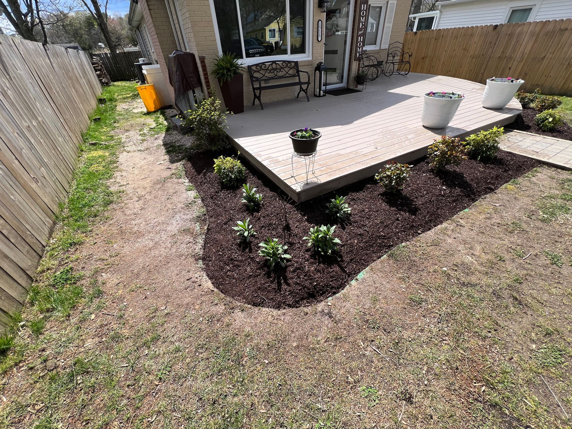 A landscaped garden bed with plants, mulch, and a concrete patio.