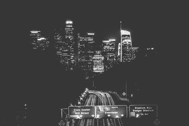 Nighttime city skyline with illuminated skyscrapers above a road leading toward downtown.
