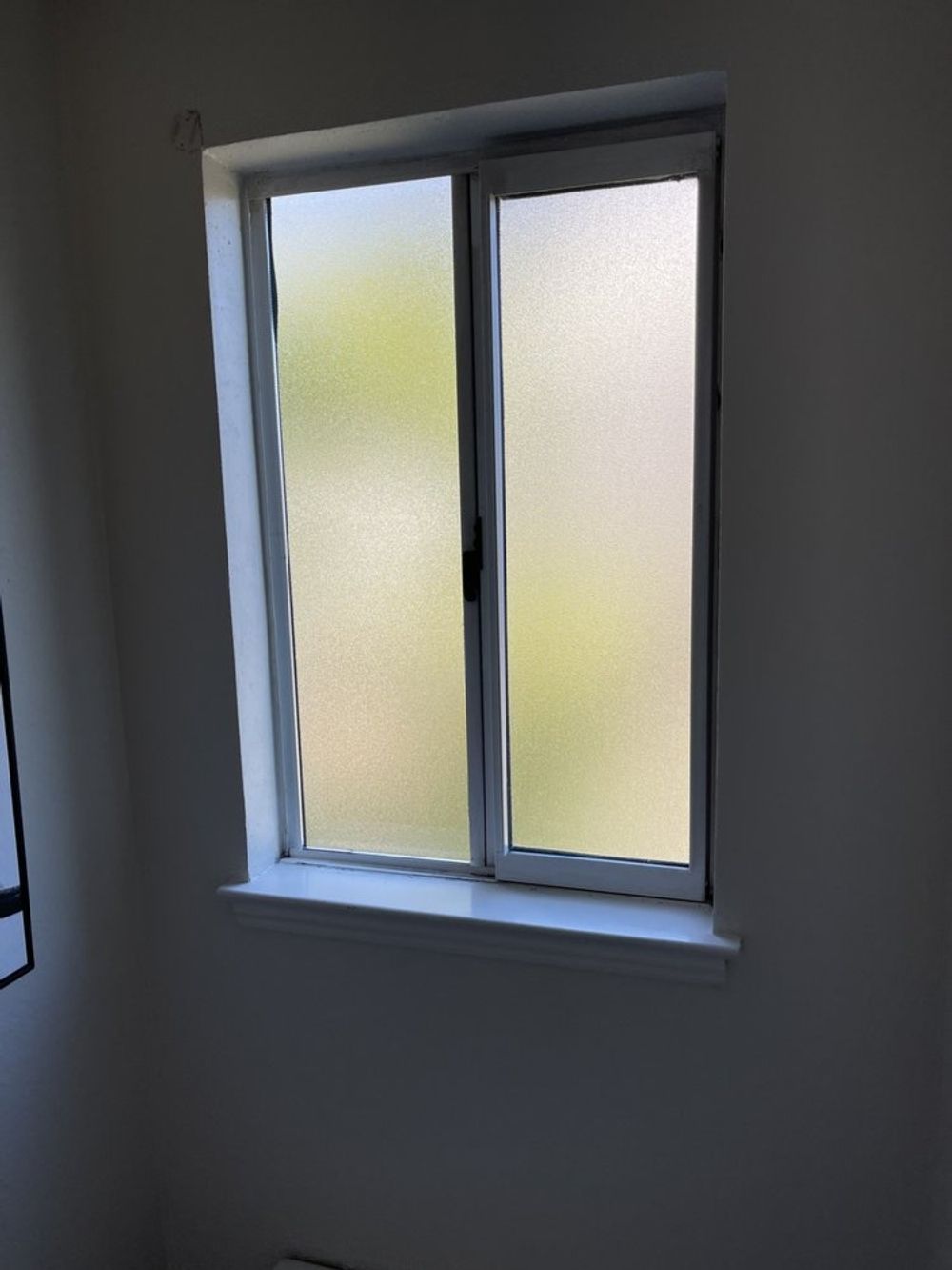 White-framed, frosted-glass window in a light-colored room, partially obscuring the outdoors.