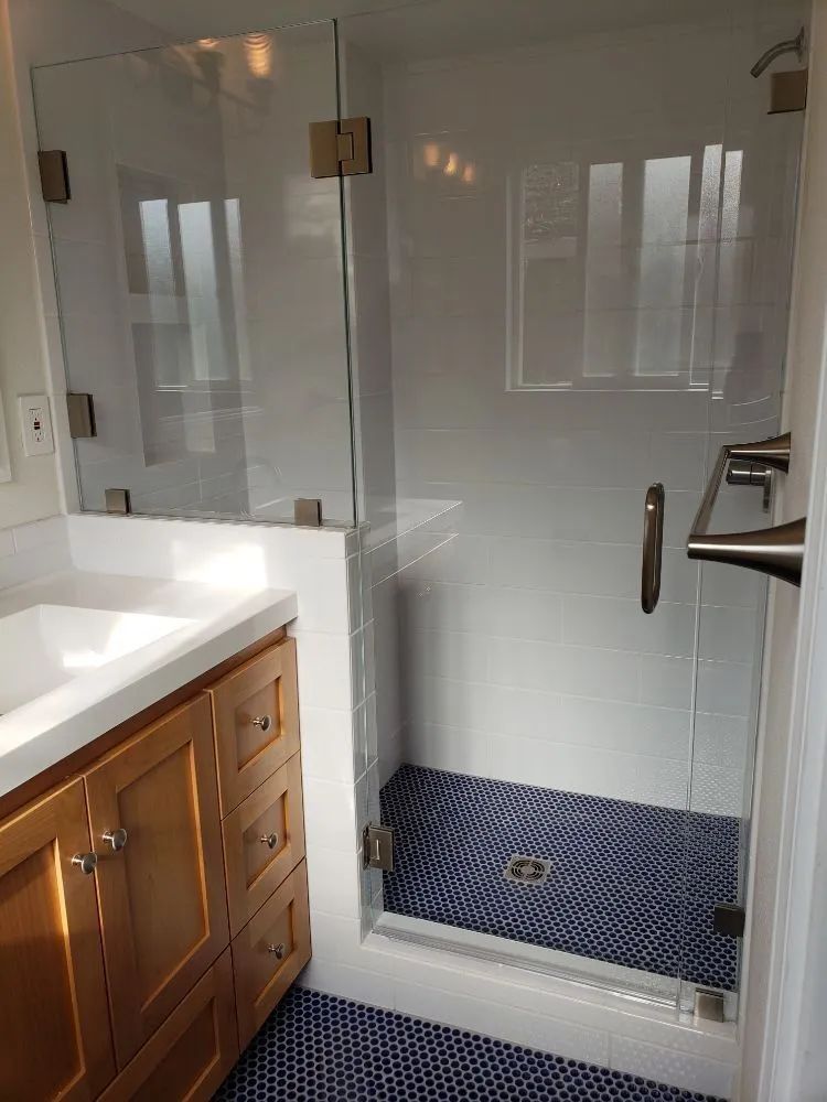 A bathroom vanity with a wooden cabinet next to a glass-enclosed shower with small dark blue circular floor tiles.