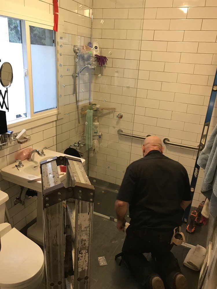 A man is kneeling in a bathroom next to a toilet and sink.