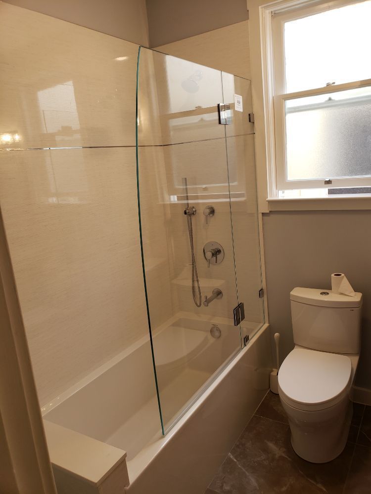 A bathroom with a toilet , bathtub , shower and window.
