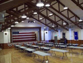 A large room with tables and chairs and an american flag on the stage