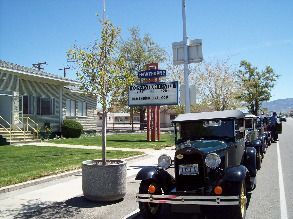 A row of old cars are parked on the side of the road in front of a building.