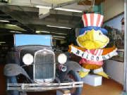 A statue of uncle sam is sitting in front of an old car.