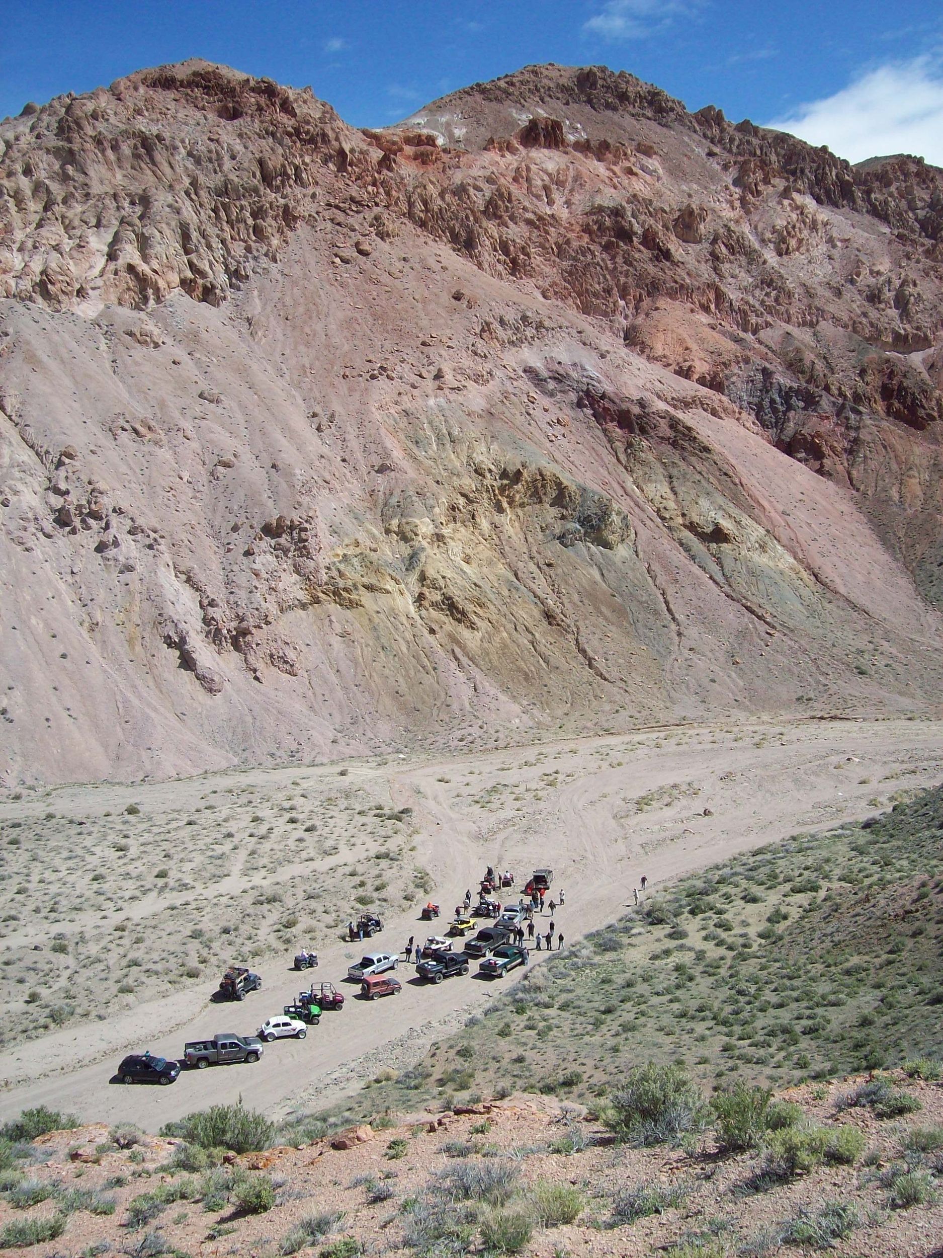 A group of cars are parked on a dirt road in front of a mountain