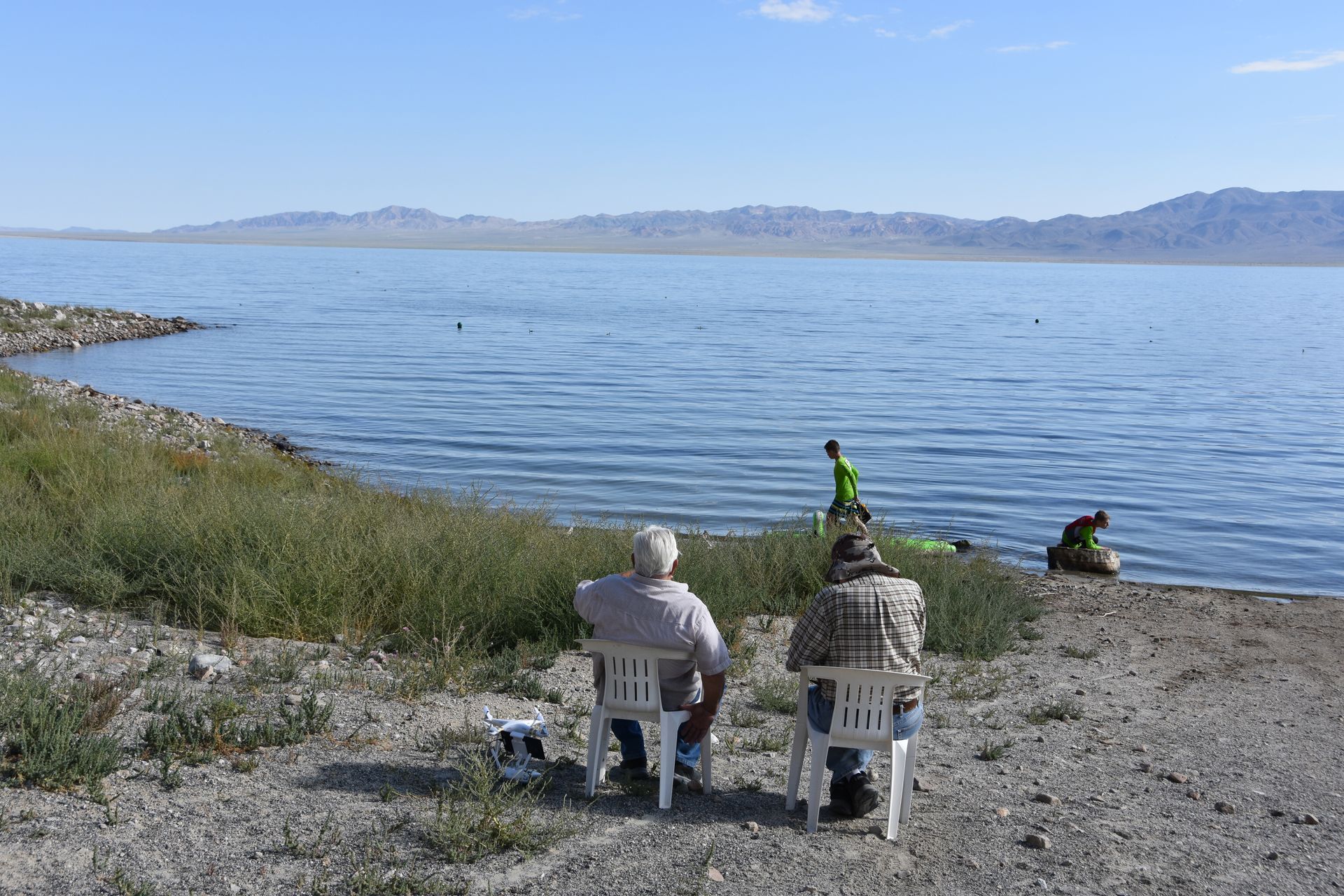 Two men are sitting on the shore of a lake
