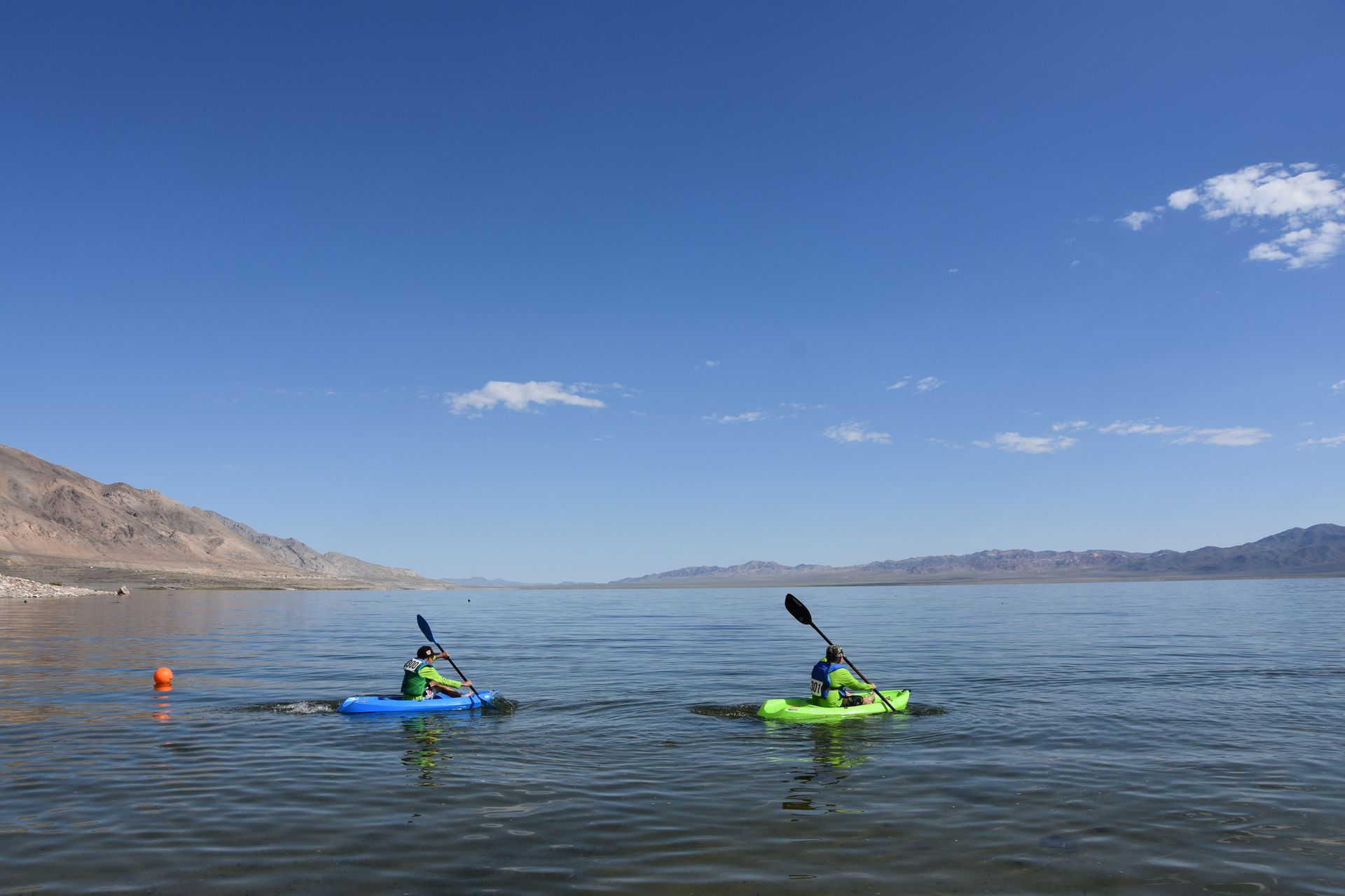 Two people are kayaking on a lake with mountains in the background.