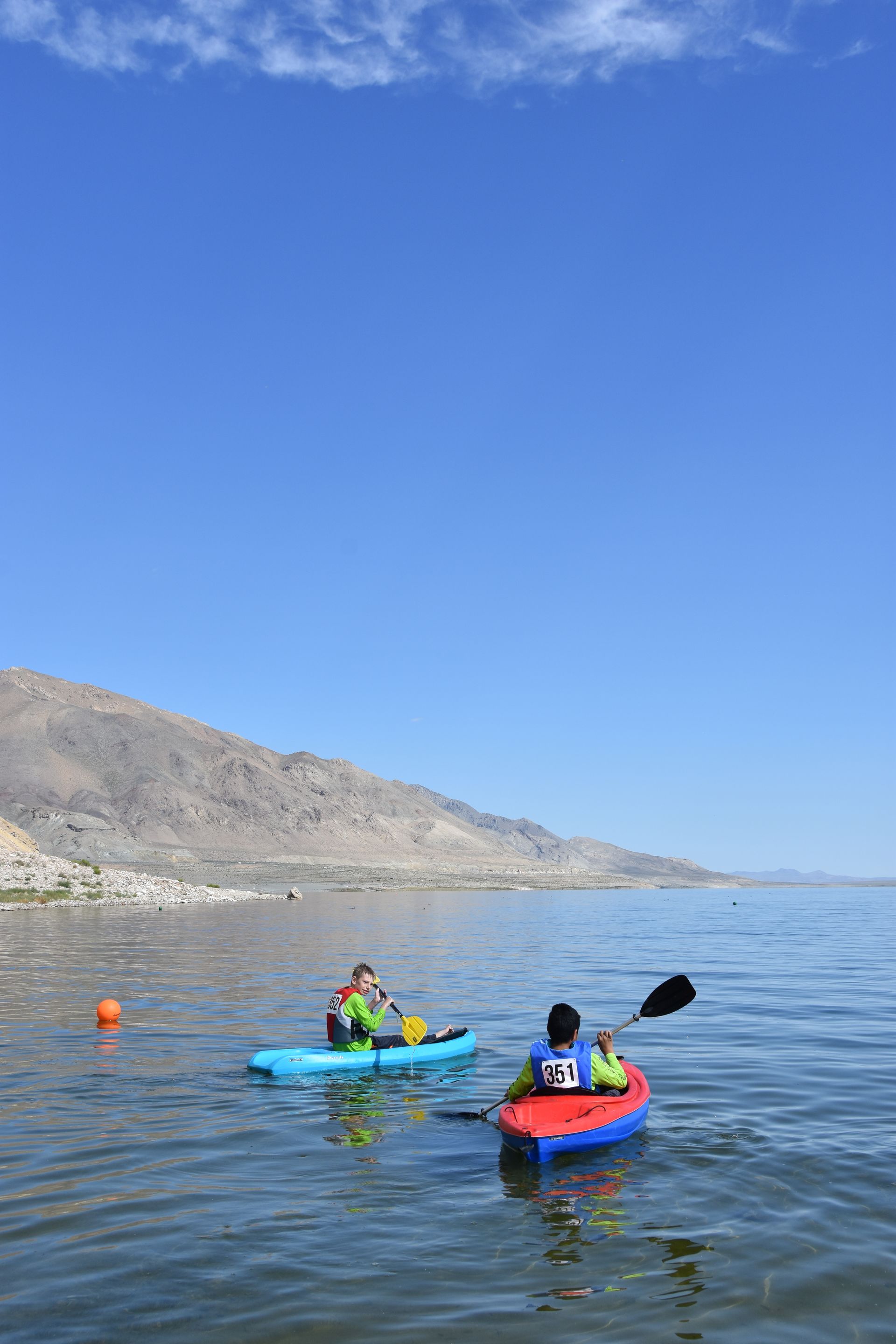 Two people are kayaking on a lake with mountains in the background.
