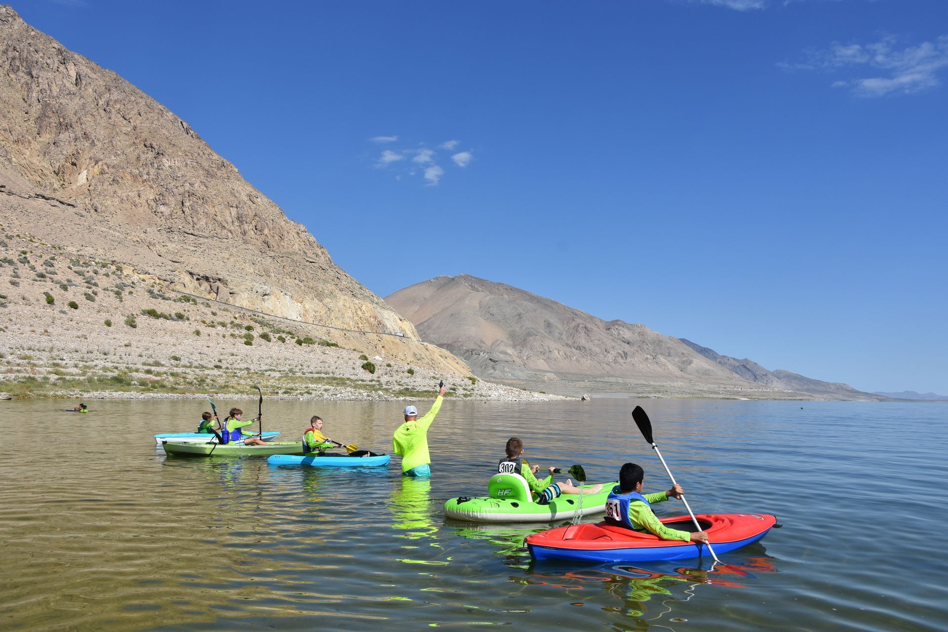 A group of people are kayaking on a lake with mountains in the background.