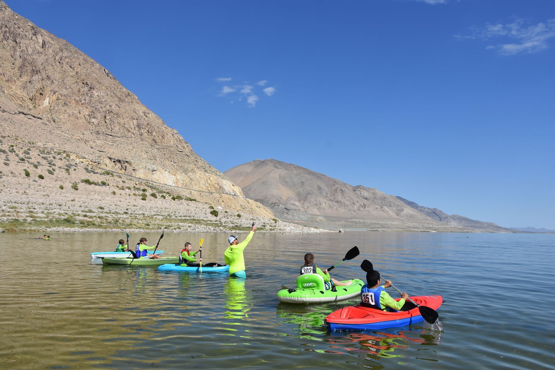 A group of people are kayaking on a lake with mountains in the background.