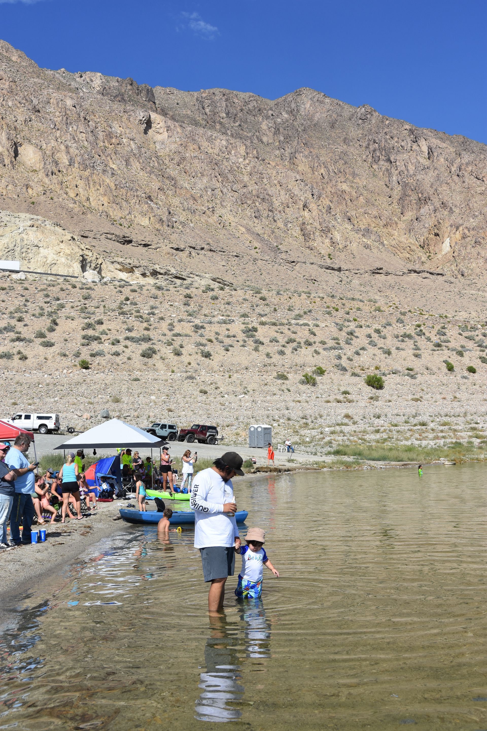 A group of people are standing in a lake with mountains in the background.