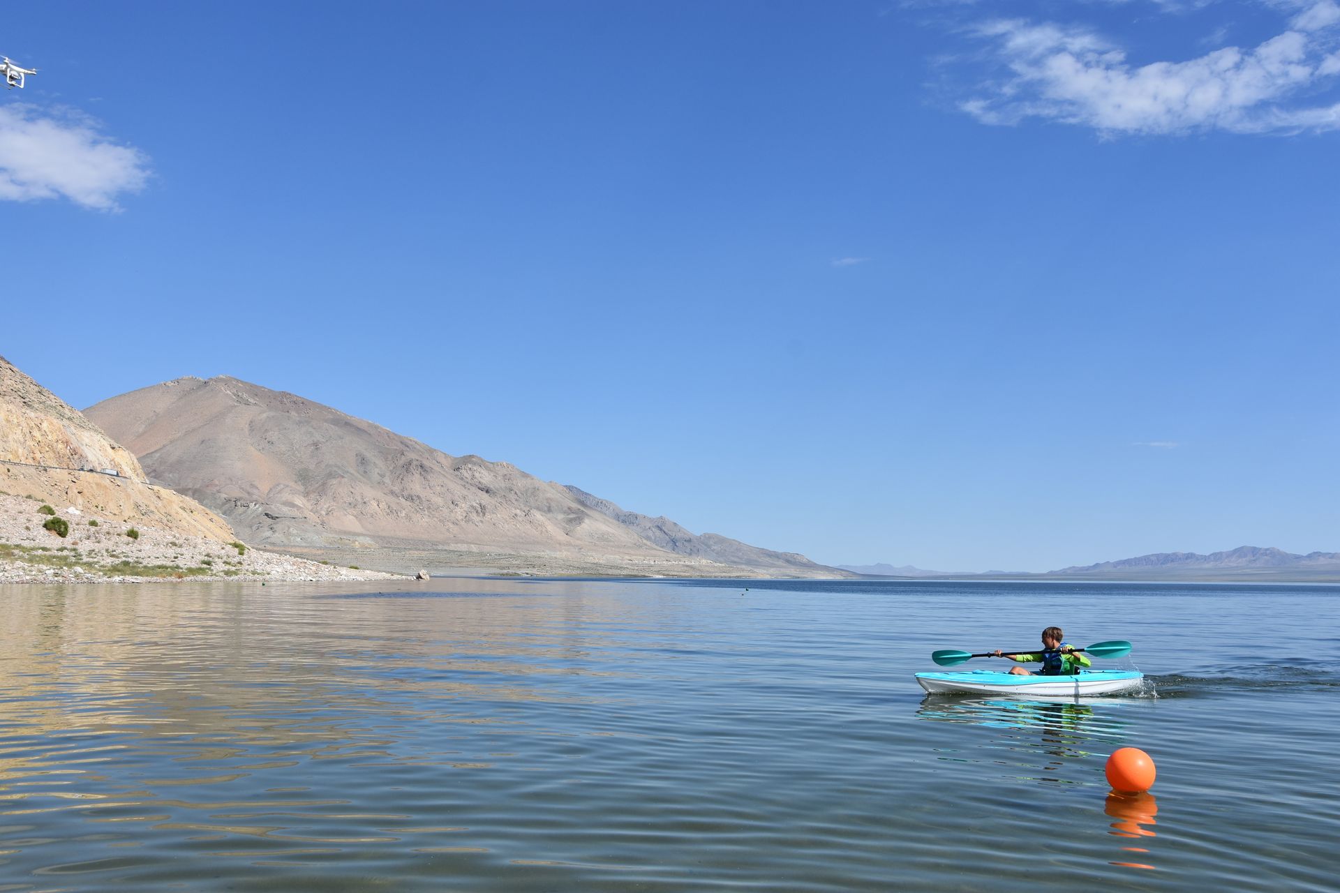 A person is kayaking on a lake with mountains in the background.