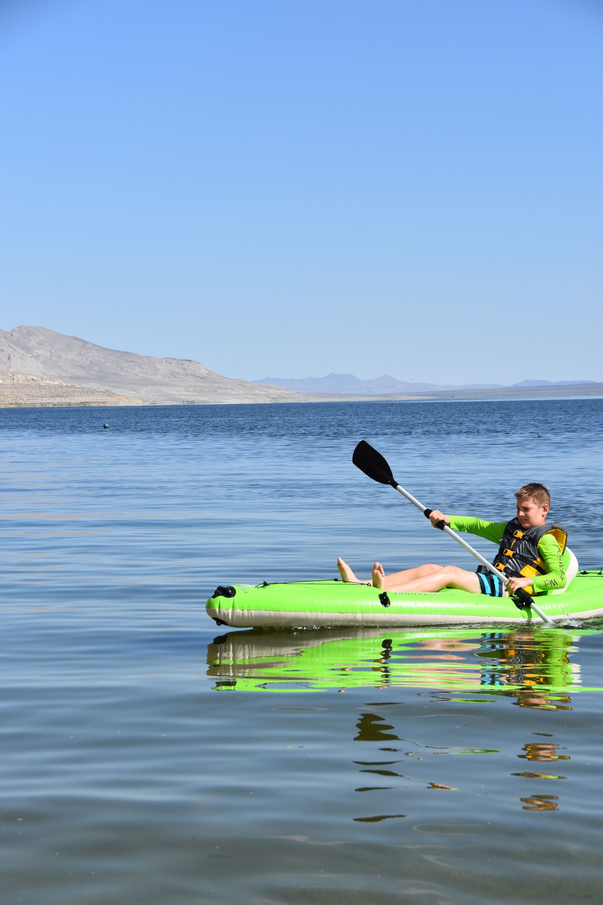 A young boy is paddling a green kayak on a lake.