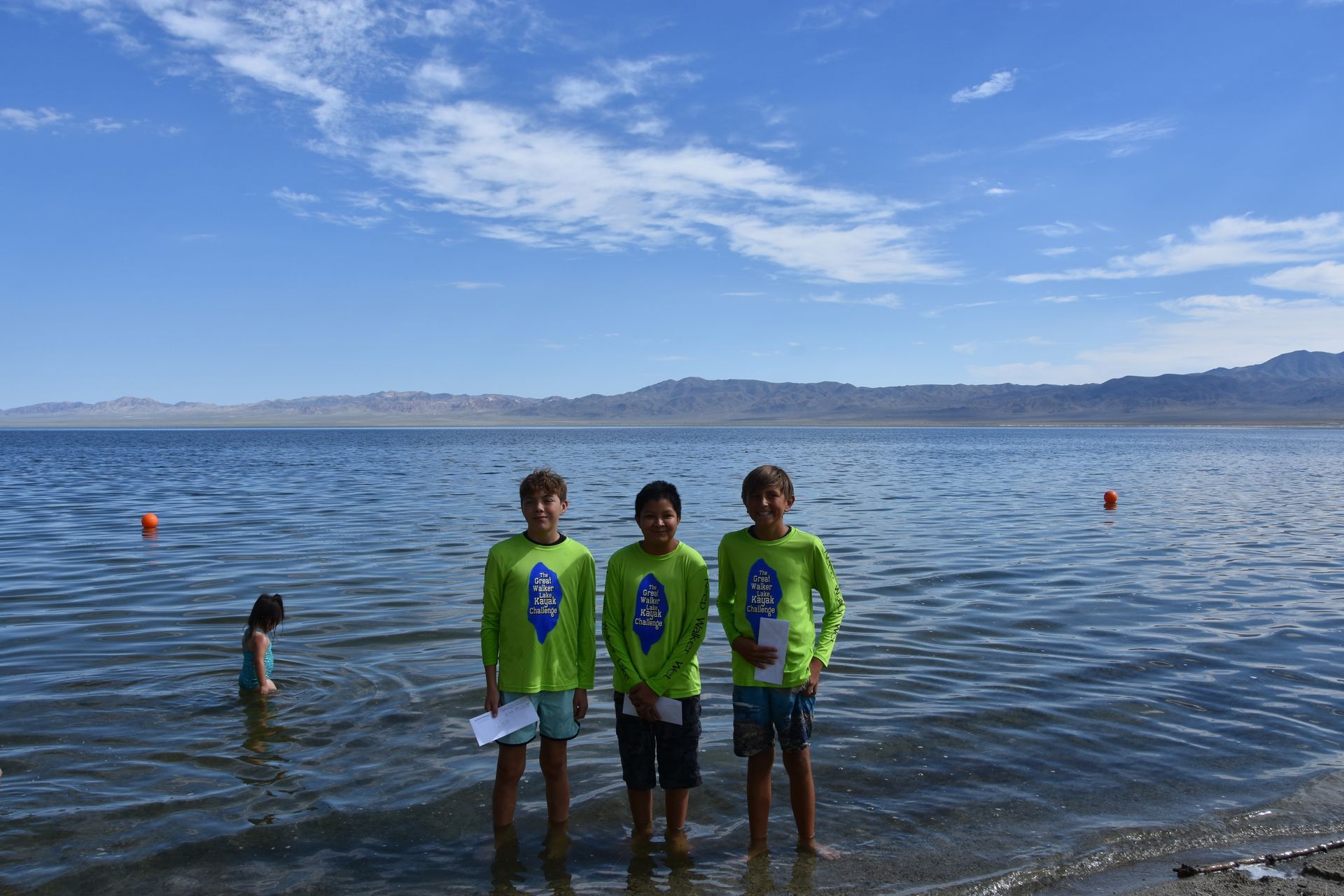 Three young boys are standing in the water on a beach.
