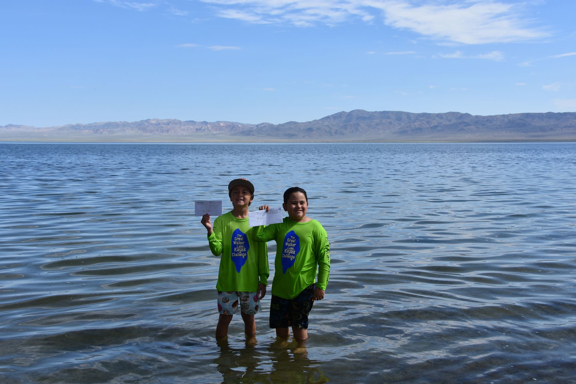 Two young boys are standing in the water holding signs.