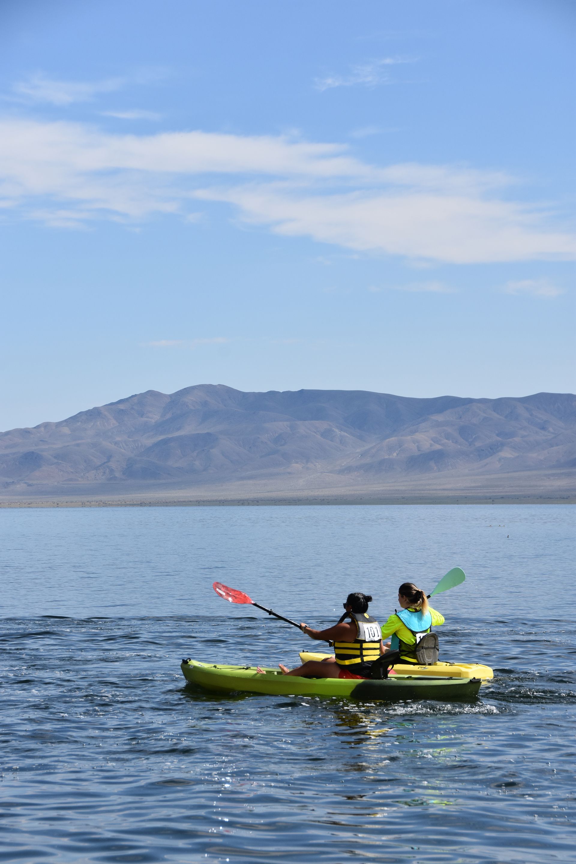Two people are kayaking on a lake with mountains in the background.