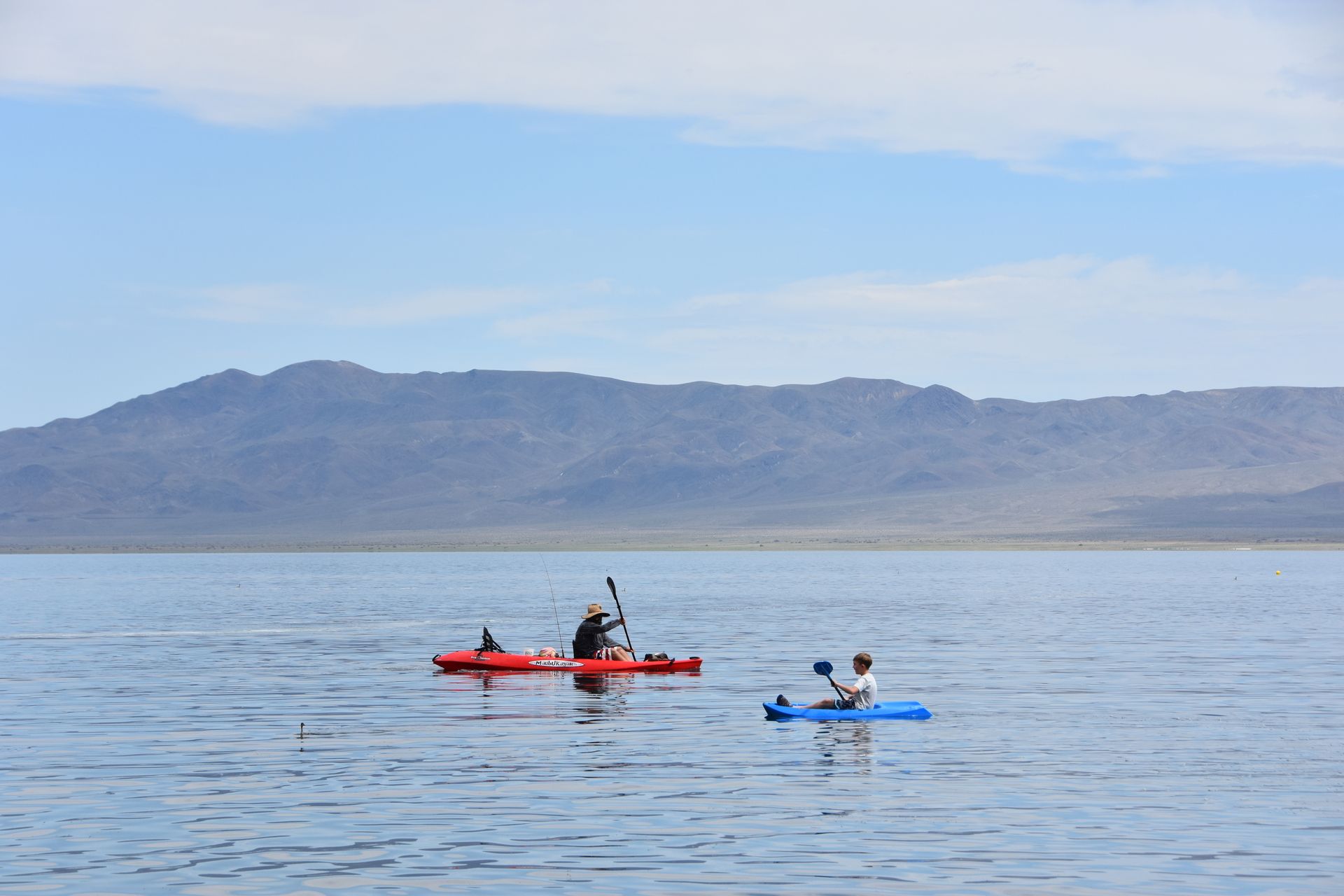 Two people in kayaks on a lake with mountains in the background