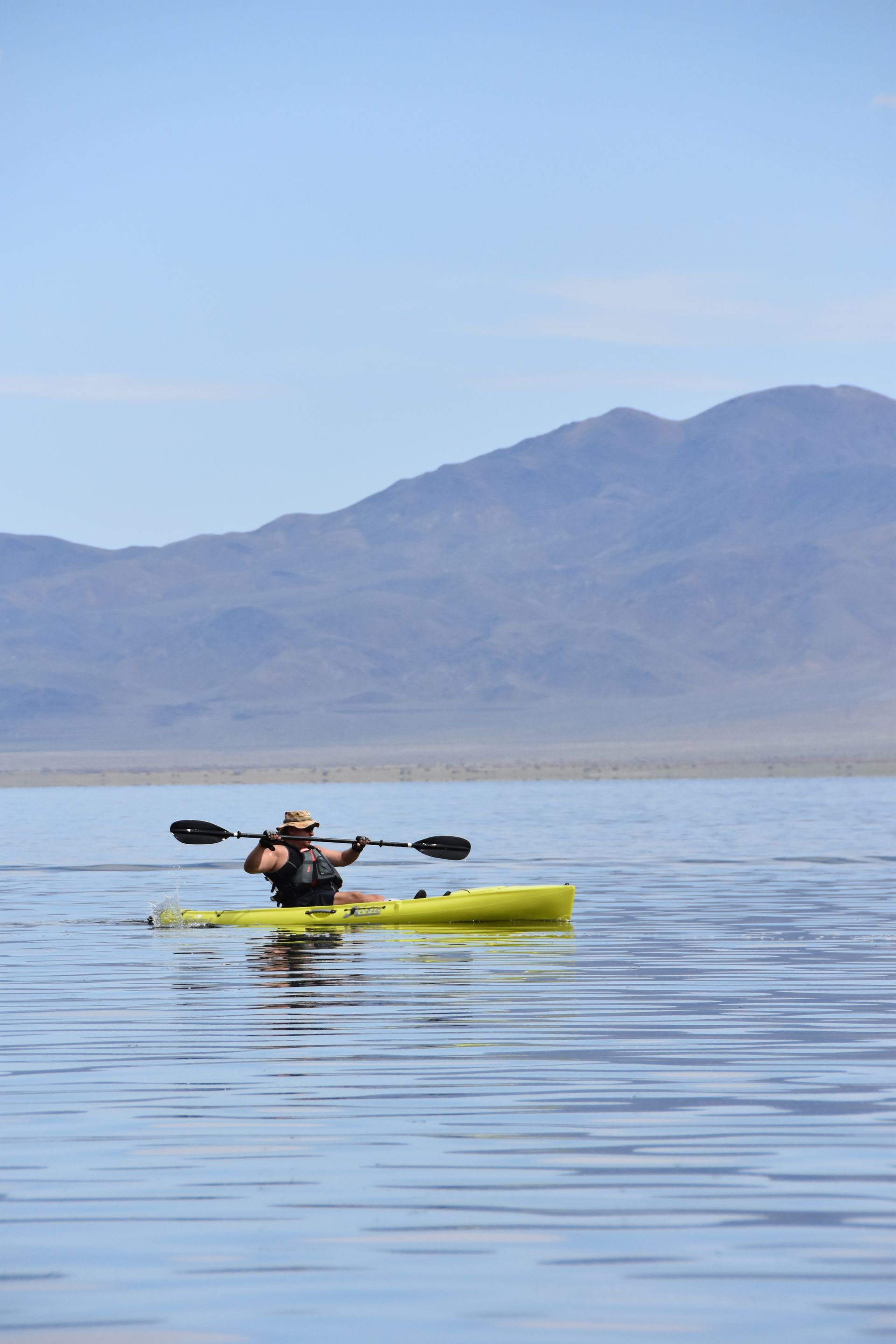 A person in a yellow kayak with mountains in the background