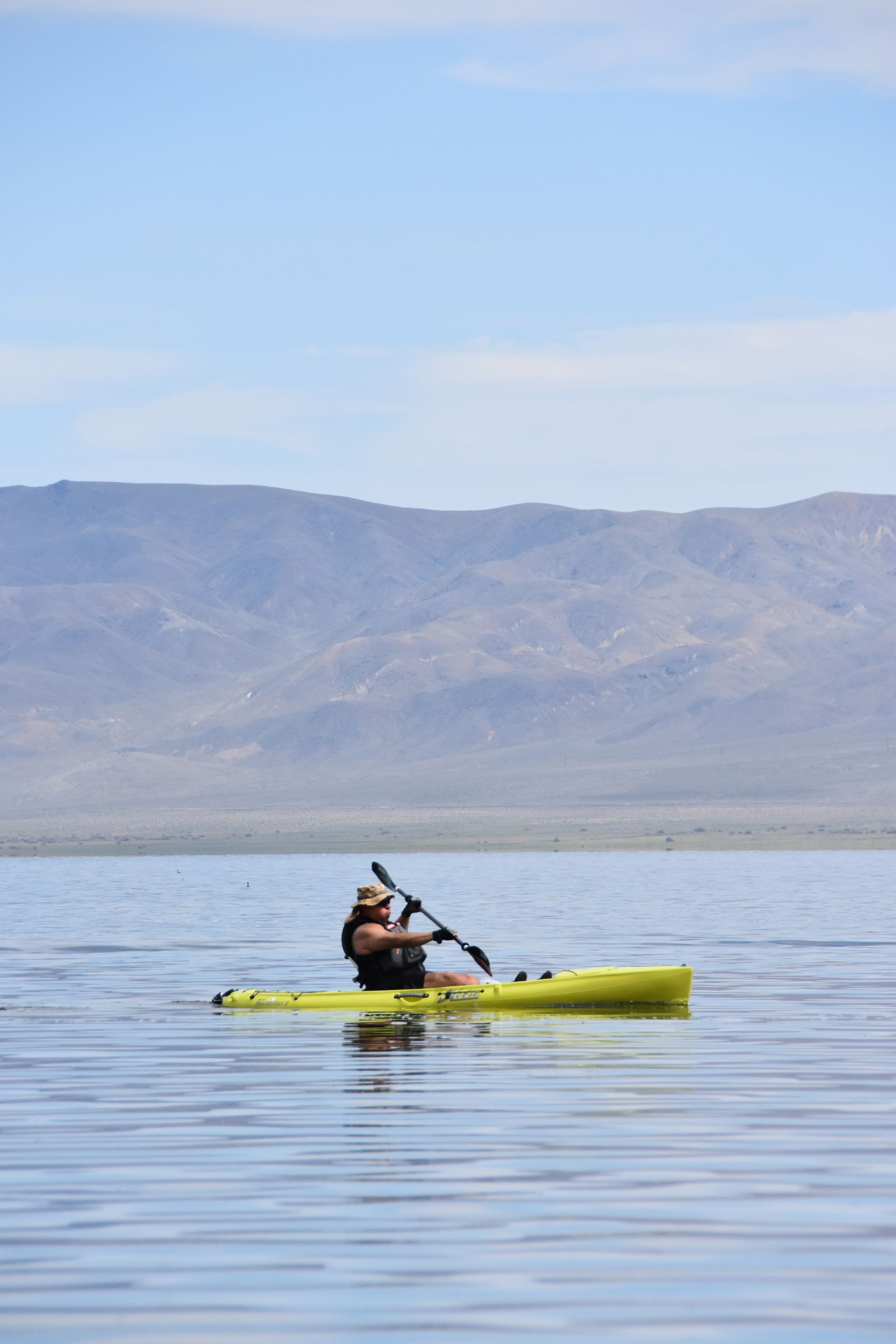 A man is paddling a yellow kayak on a lake