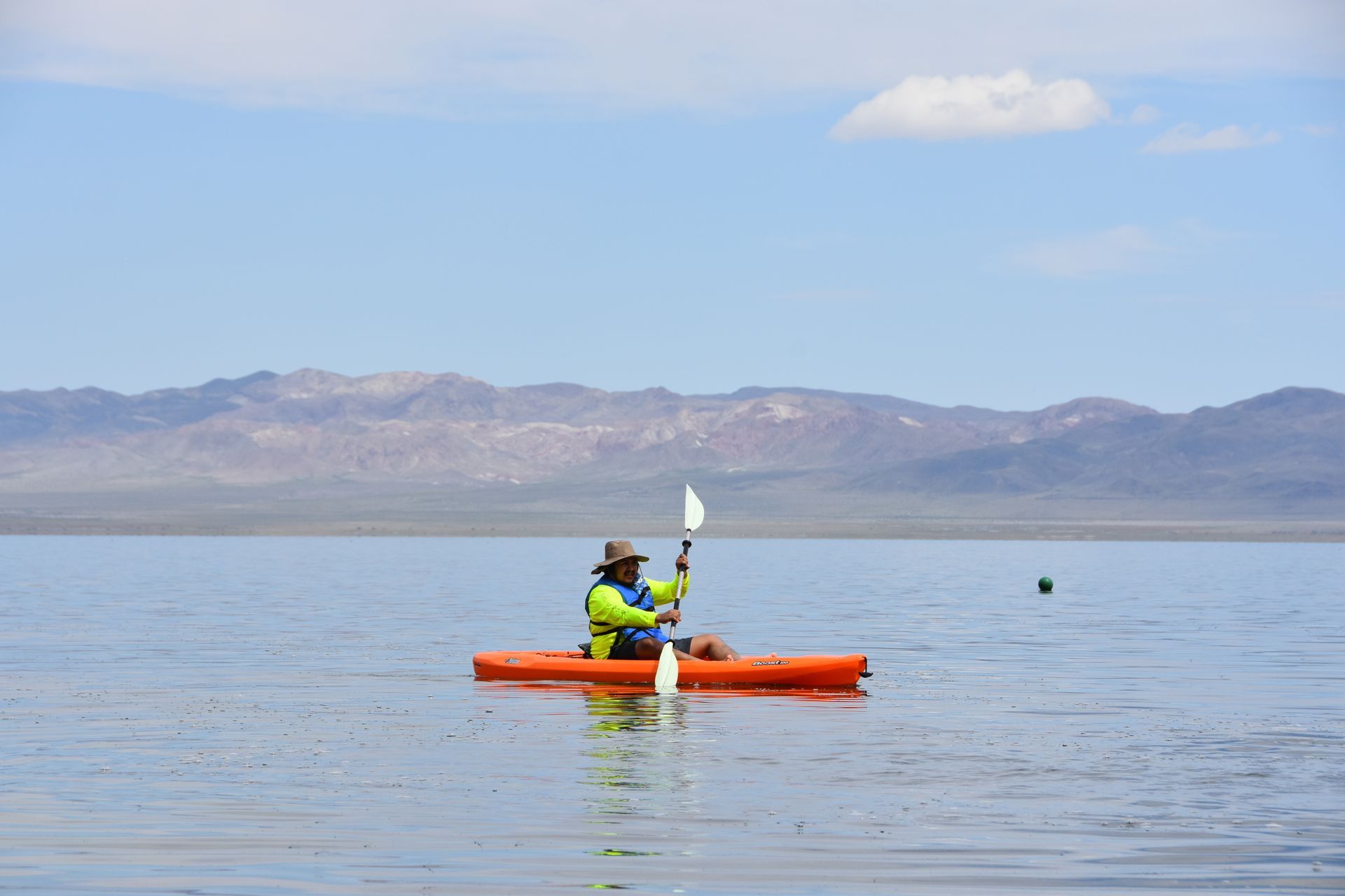 A person is paddling an orange kayak on a lake with mountains in the background.