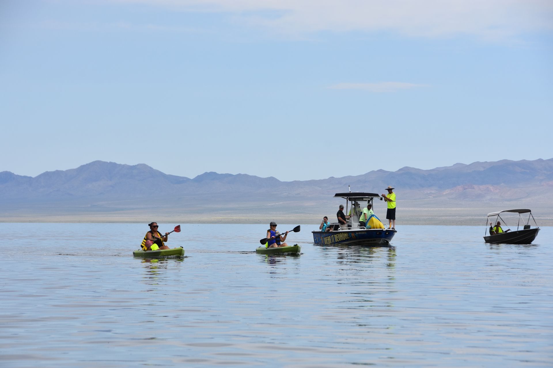A group of people in kayaks and boats are floating on a lake.