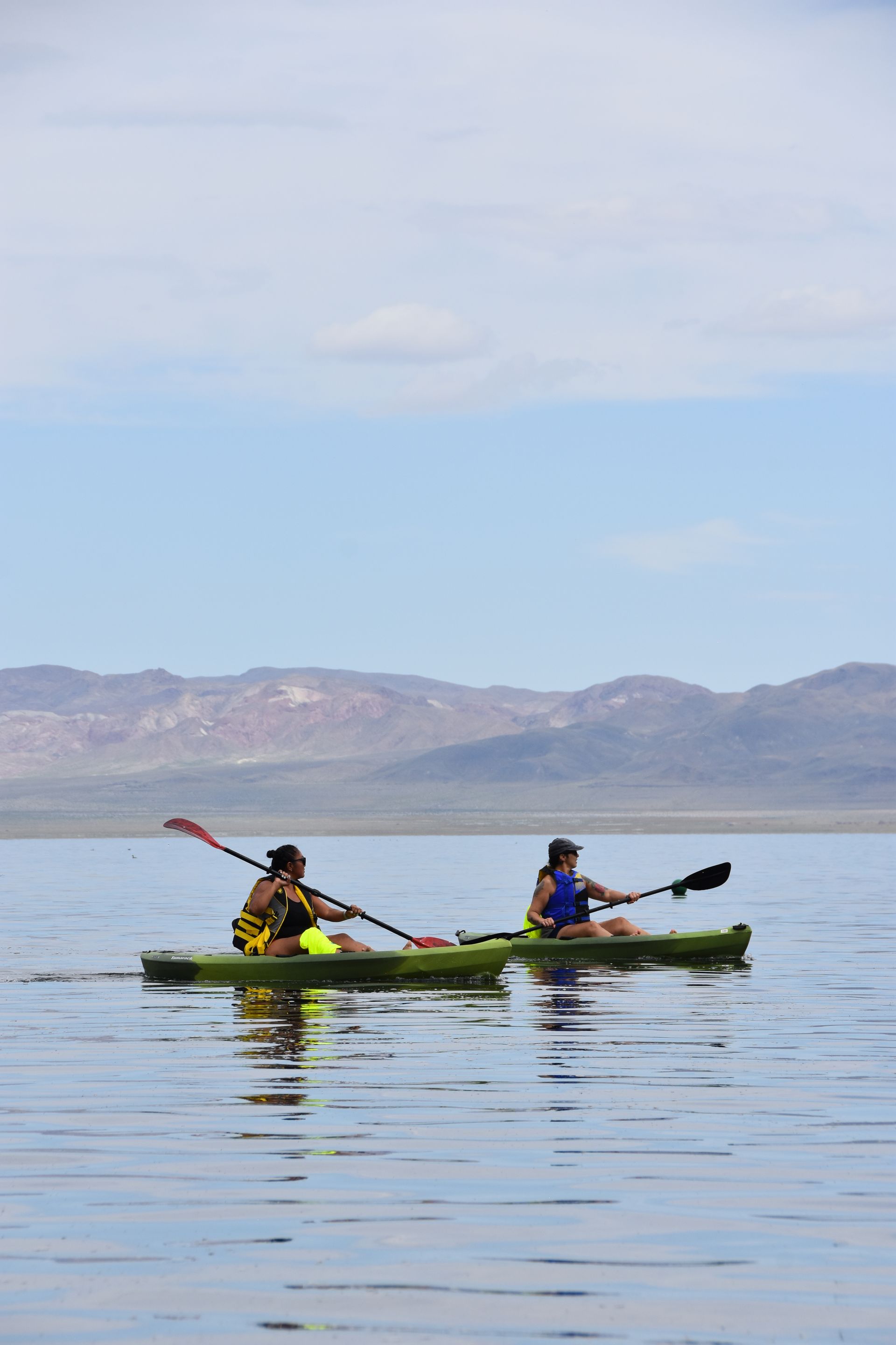 Two people are kayaking on a lake with mountains in the background.