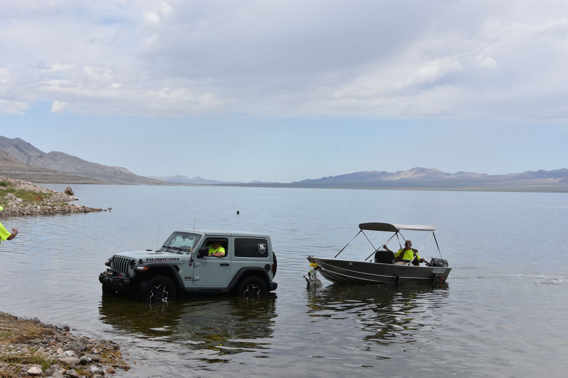 A jeep and a boat are in the water near the shore.