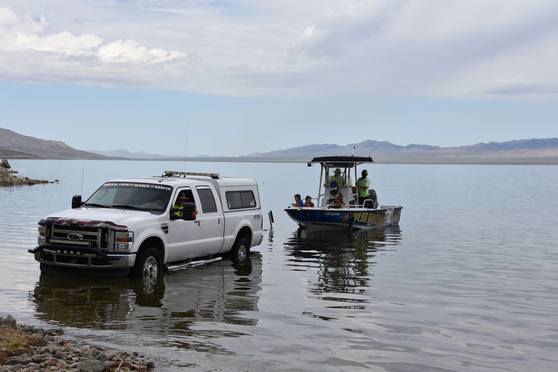 A white truck is towing a boat in the water.