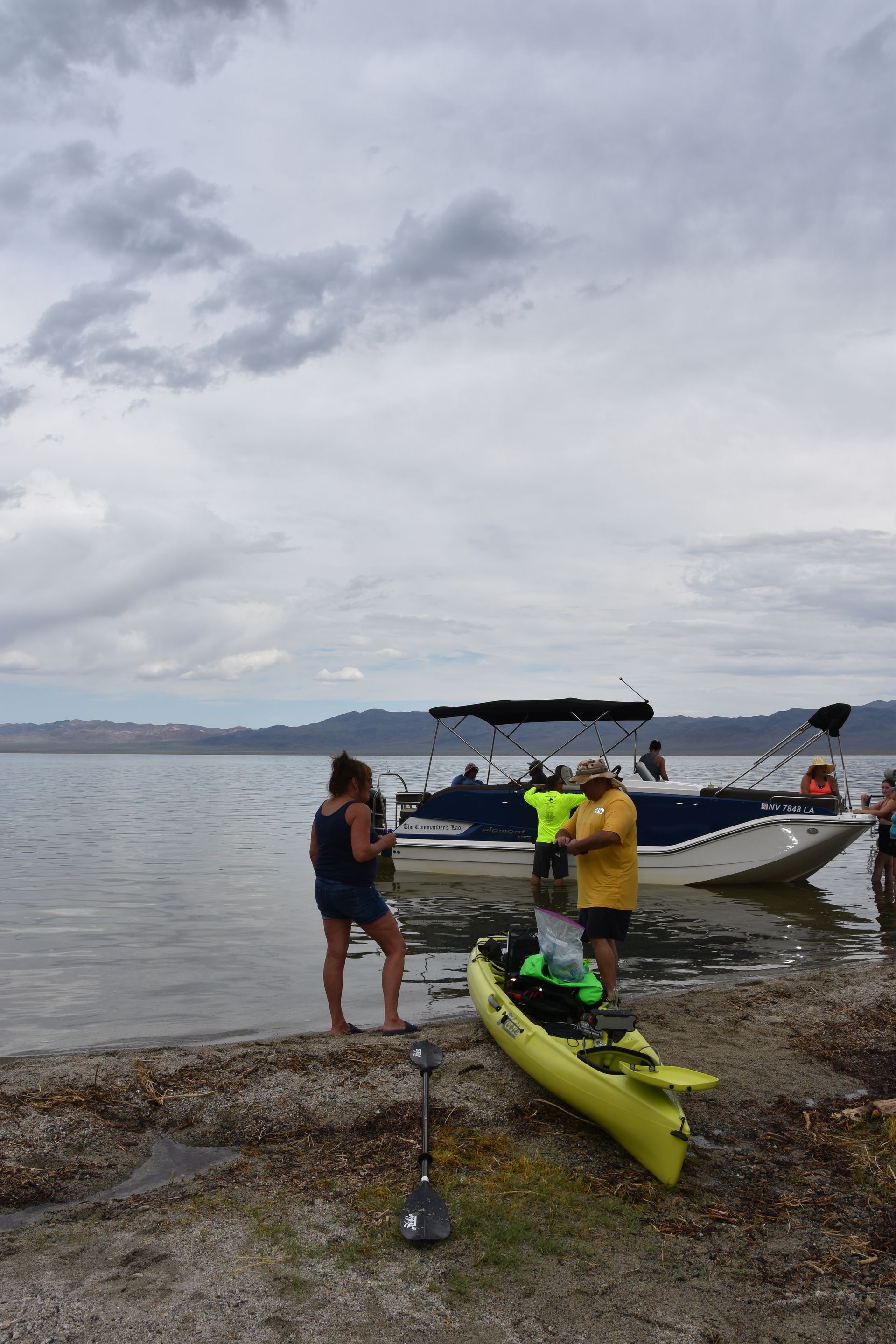 A group of people are standing on a beach next to a boat and a kayak.