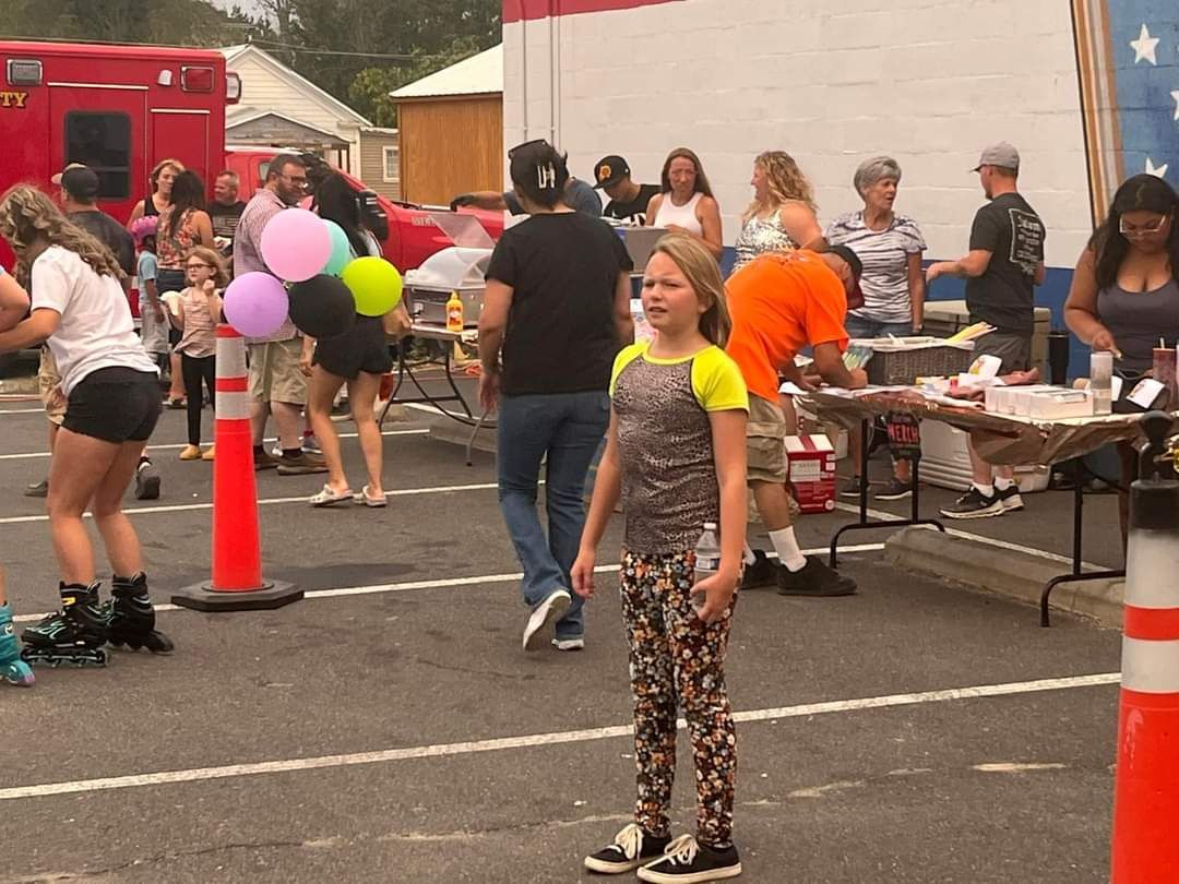 Girl in sparkly top watching Skate Night 2024 in Mineral Co, NV. Other people, balloons, & a fire truck in the background.