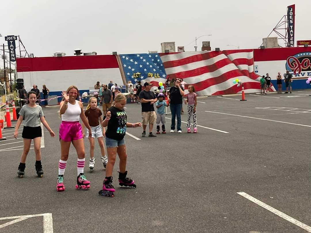 A group of people are rollerblading in a parking lot in front of an american flag.