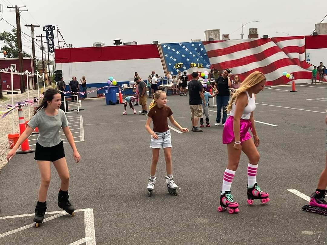 A group of young girls are rollerblading on a street in front of an american flag.