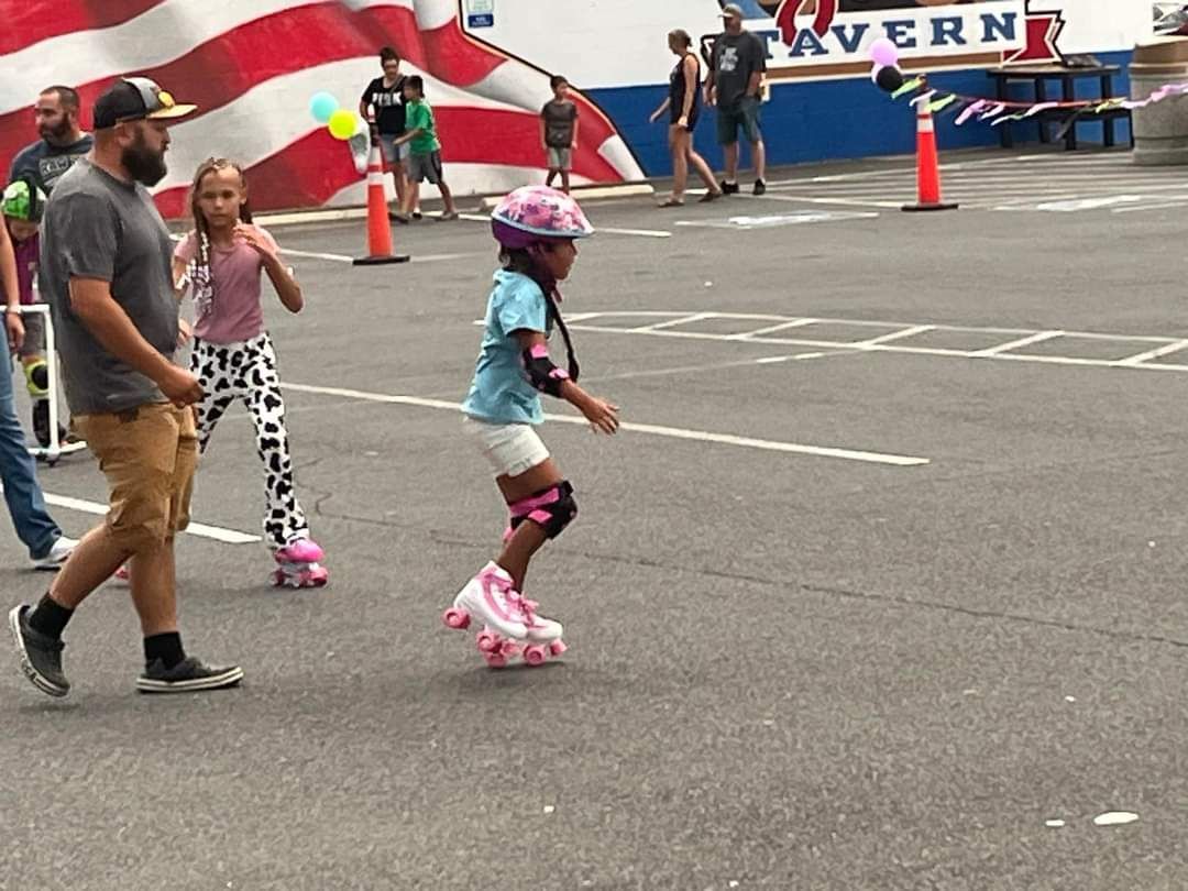 A young roller skaters during Skate Night in Hawthorne, NV. She's wearing a helmet & pads, with an adult & a skater nearby.