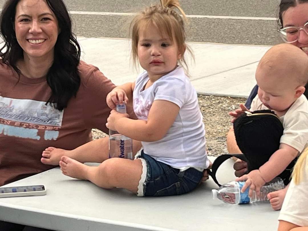 A woman and children sit at a table watching Skate Night in Mineral County, Nevada. A toddler holds a water bottle.