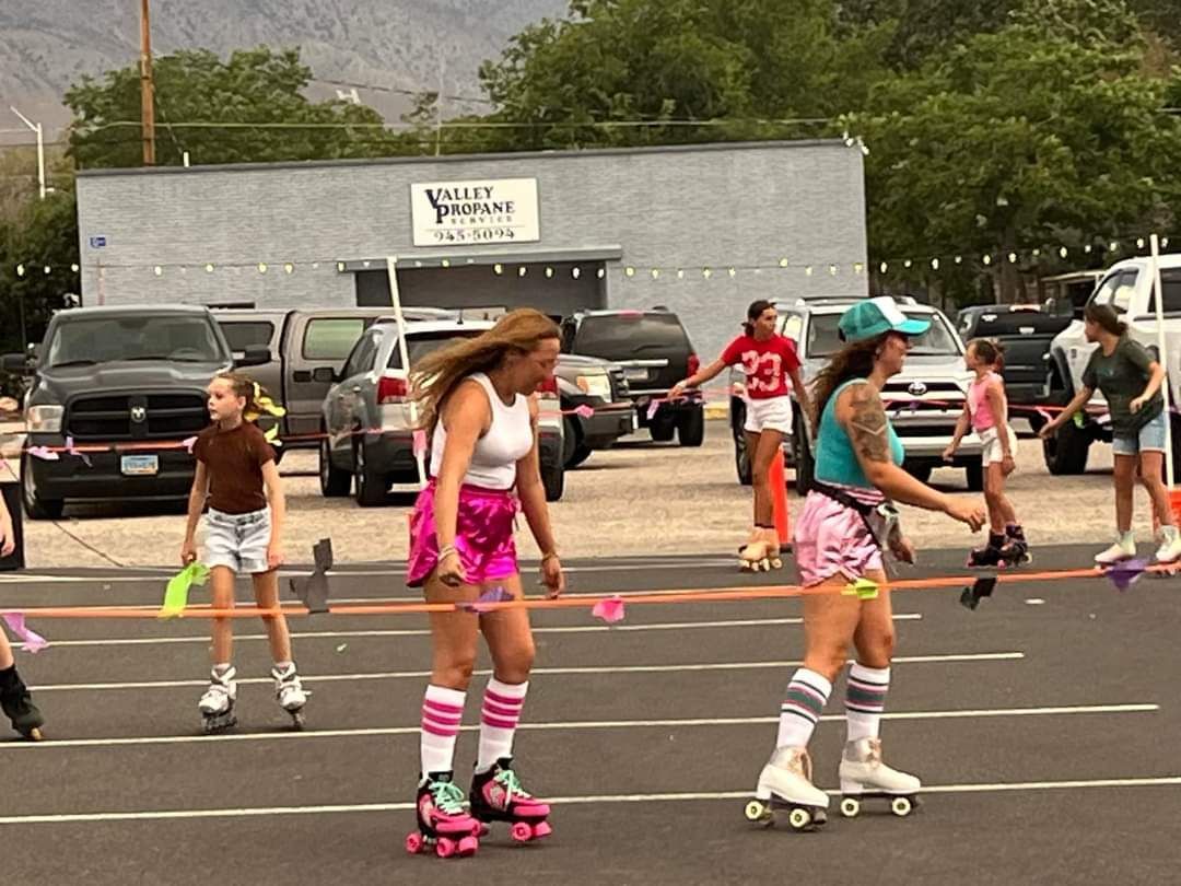 People on roller skates at the Skate Night 2024. Some wear pink skirts and shorts with cars and a building behind them.