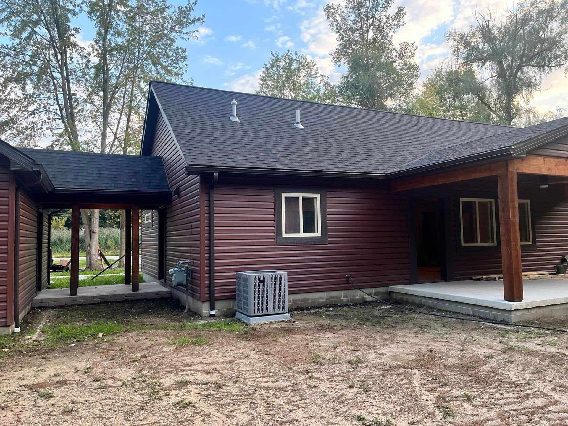 The back of a log cabin with a porch and a black roof.