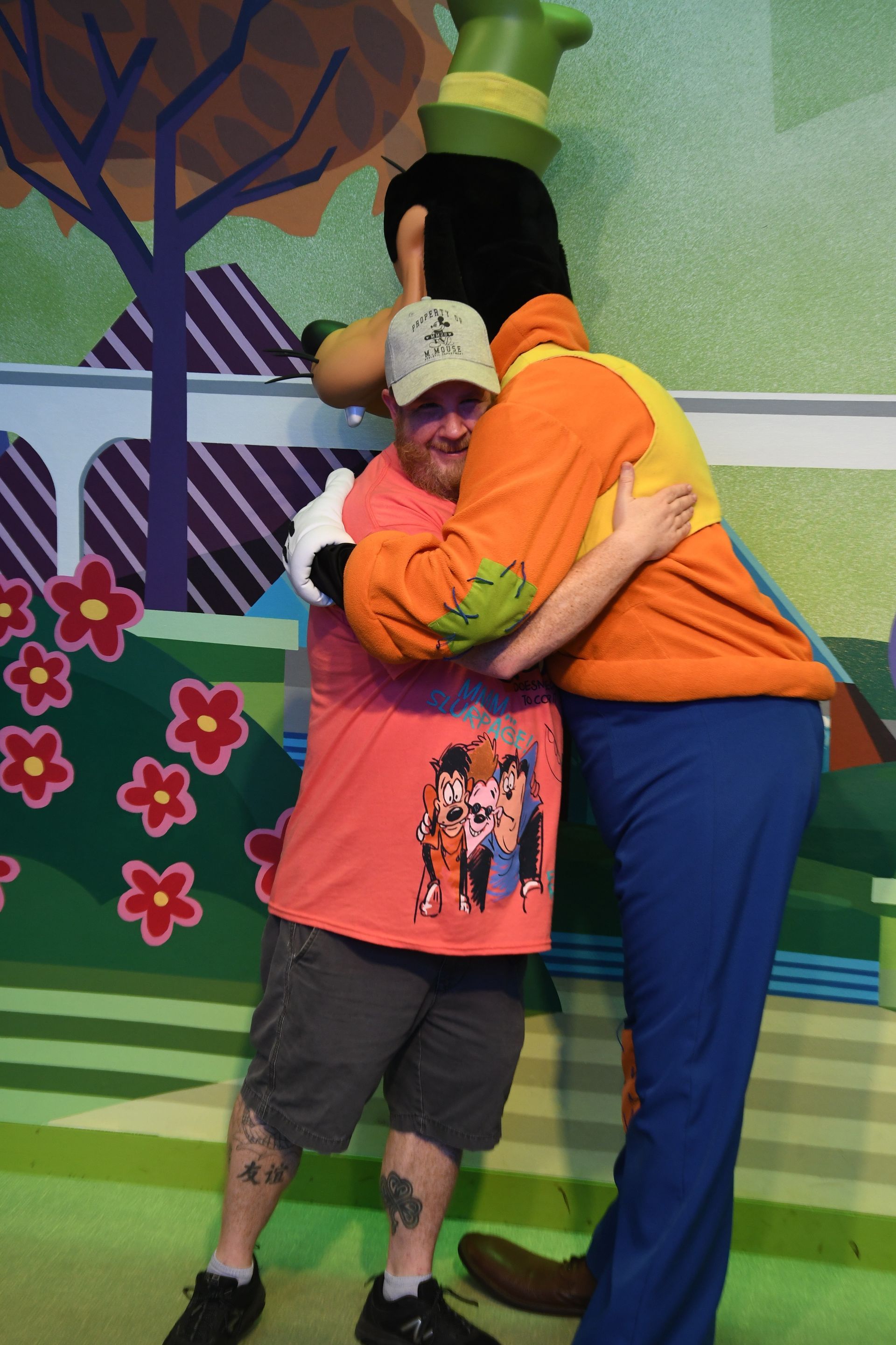 Brett of Magic Map Getaways hugging Goofy character in front of a colorful mural.