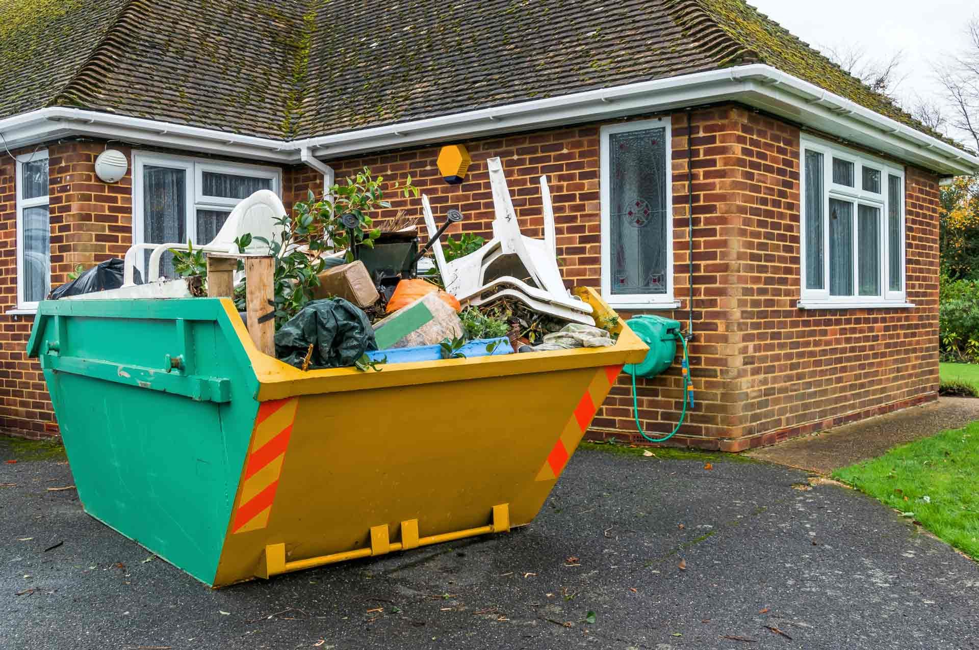 A dumpster filled with trash is parked in front of a brick house.