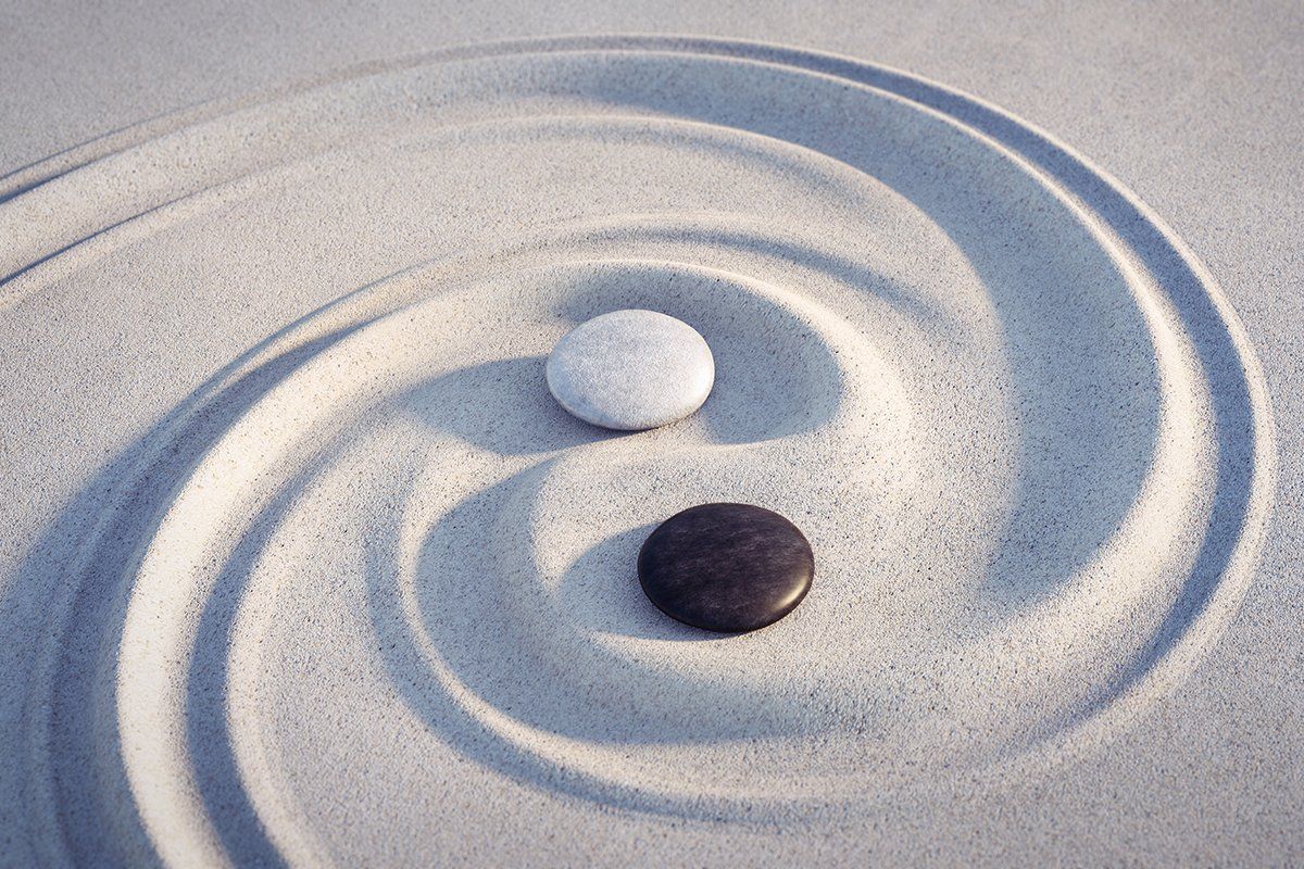 Yin-yang symbol created with 2 pebbles - a white and a black - placed over a swoosh in sand.