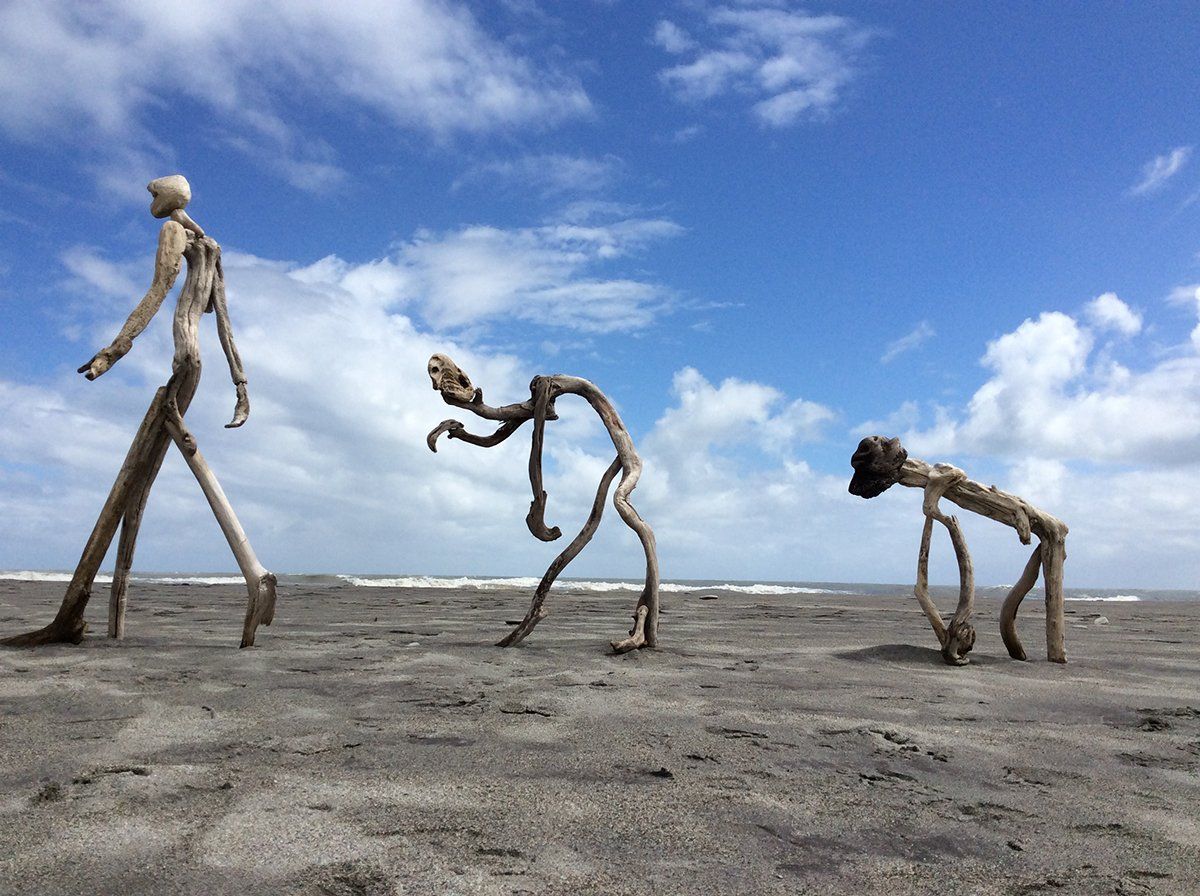 3 figures constructed from twisted driftwood emerge from the sand