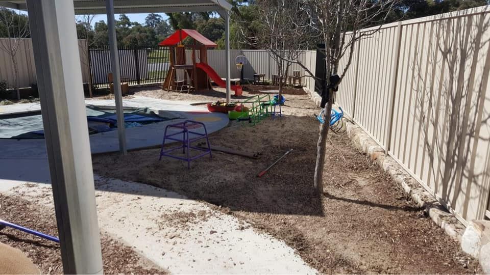 A playground with a fence and a red house in the background