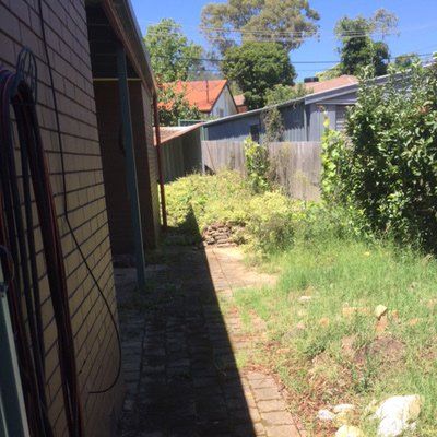 A brick walkway leading to a house with a fence in the background.